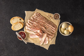Strips of Opa's Smoked Peppered Bacon on a board with bread and eggs