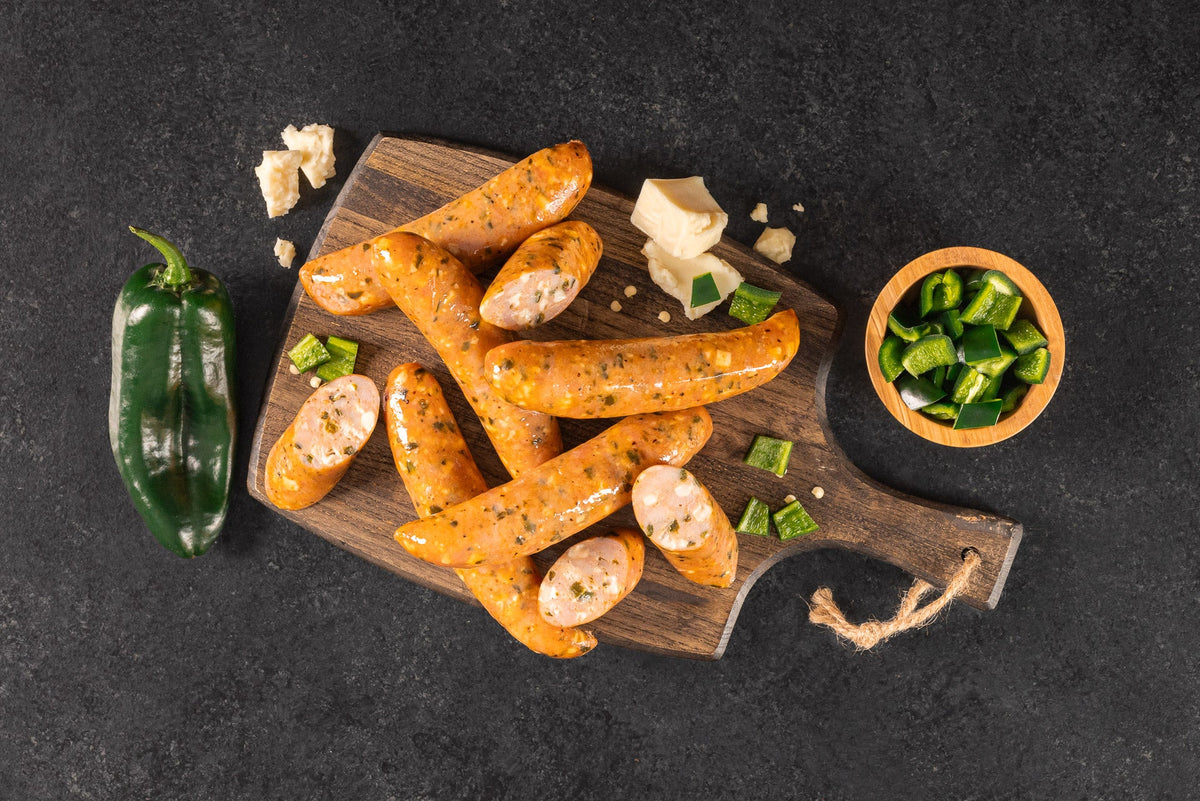 Opa's Chicken Poblano Monterey Jack Smoked Sausage links, whole and sliced, on a wooden board with a poblano pepper