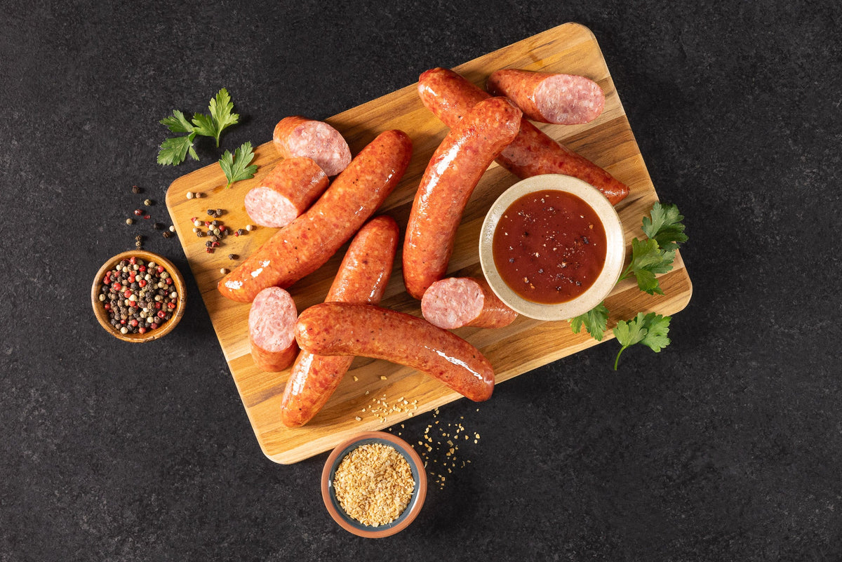 Opa's Country Blend Smoked Sausage links, whole and sliced, on a wooden board with a dipping sauce and spices