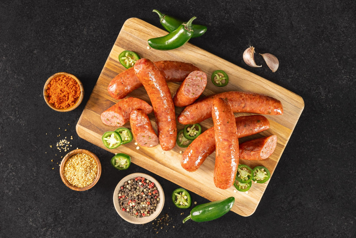 Opa's Jalapeño Smoked Sausage links, whole and sliced, on a wooden board with jalapeños