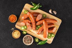 Opa's Jalapeño Smoked Sausage links, whole and sliced, on a wooden board with jalapeños
