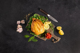 Opa's whole smoked chicken on a cutting board with lemon, herbs, garlic and tomatoes