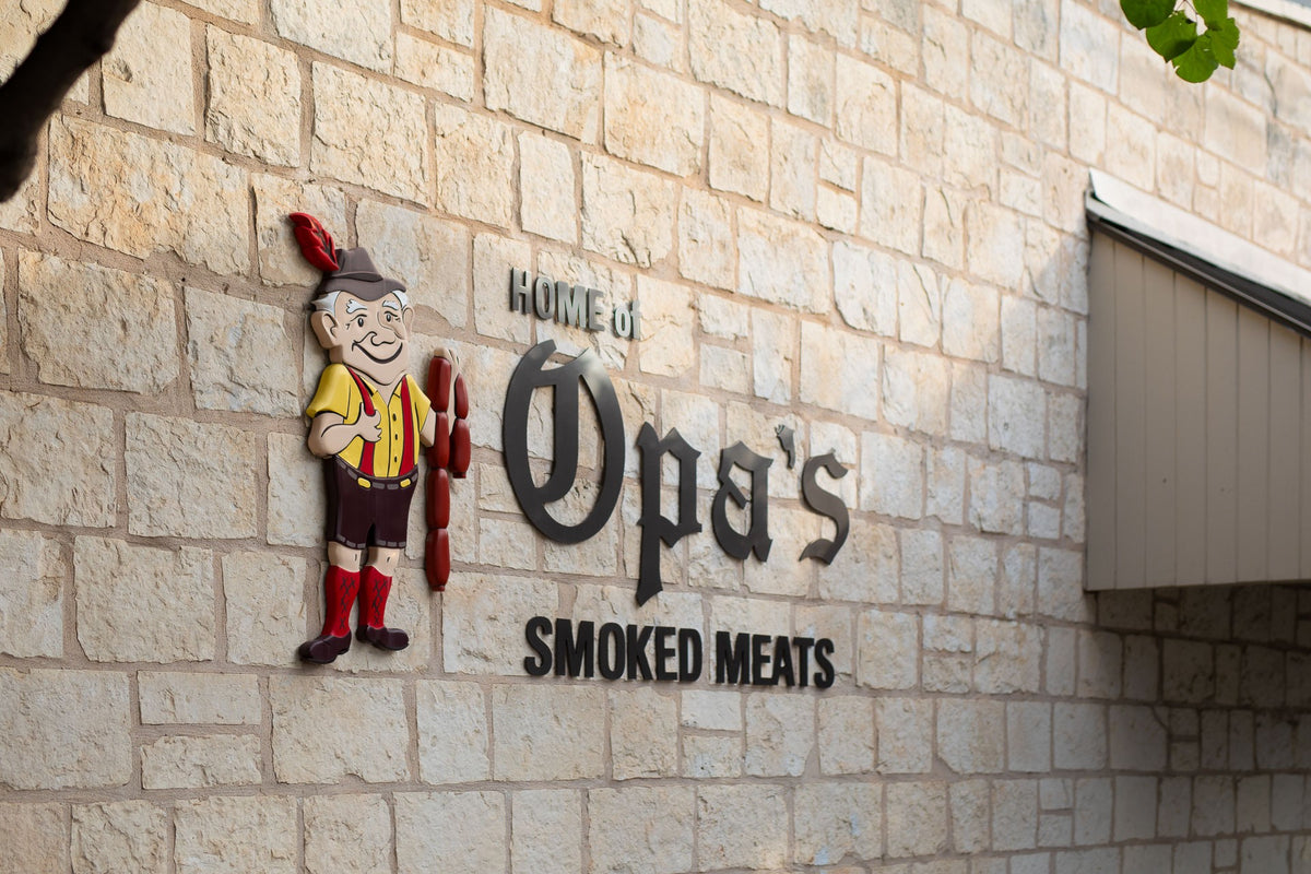 The Home of Opa's Smoked Meats sign with Opa holding a string of sausage links, on the limestone wall on Washington Street